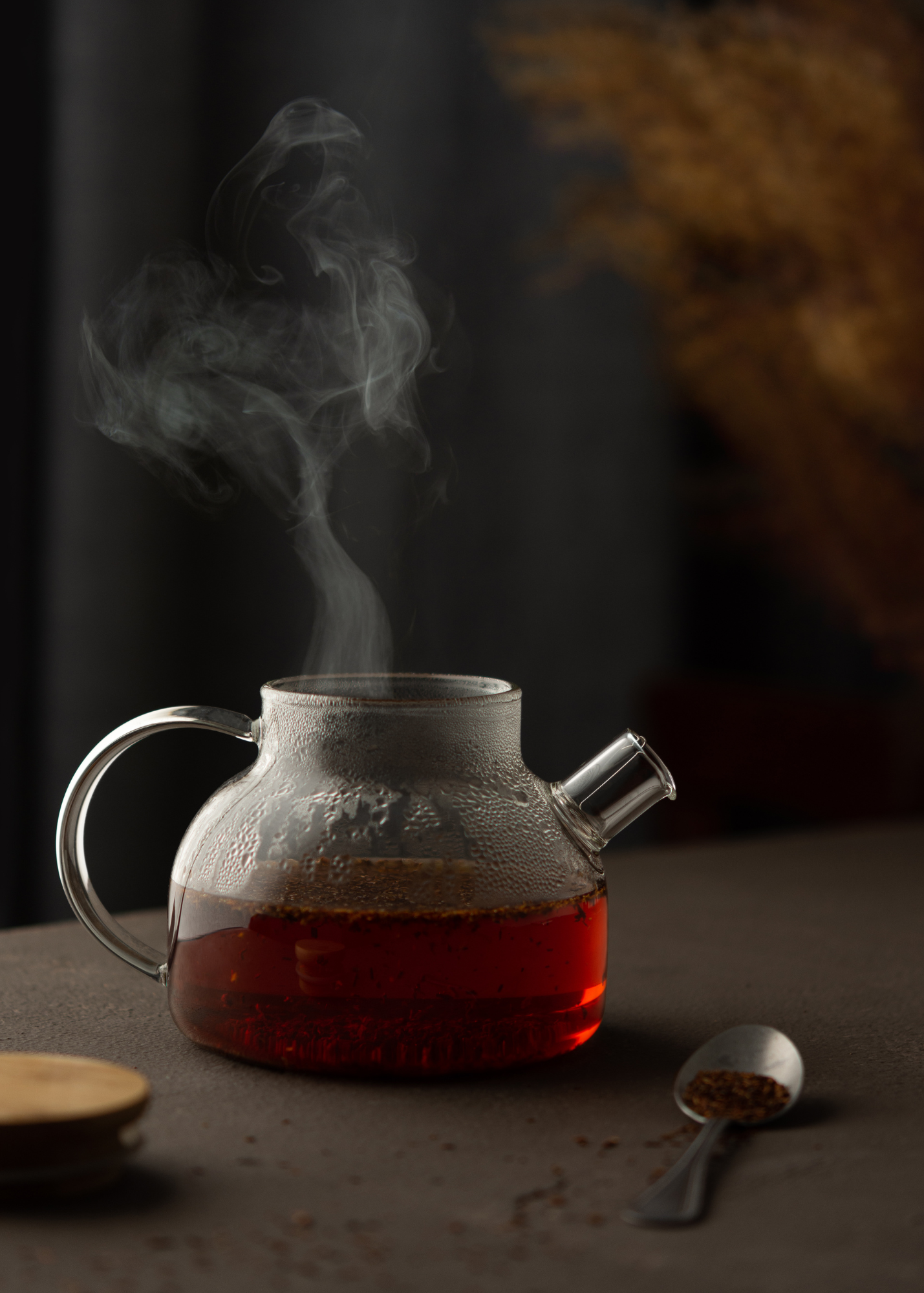 A clear teapot with the lid off and steaming in a dark room