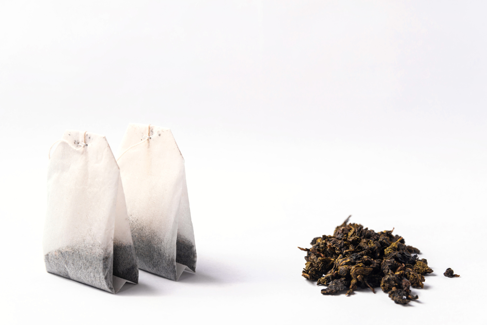 Two tea bags next to a small pile of loose leaf tea