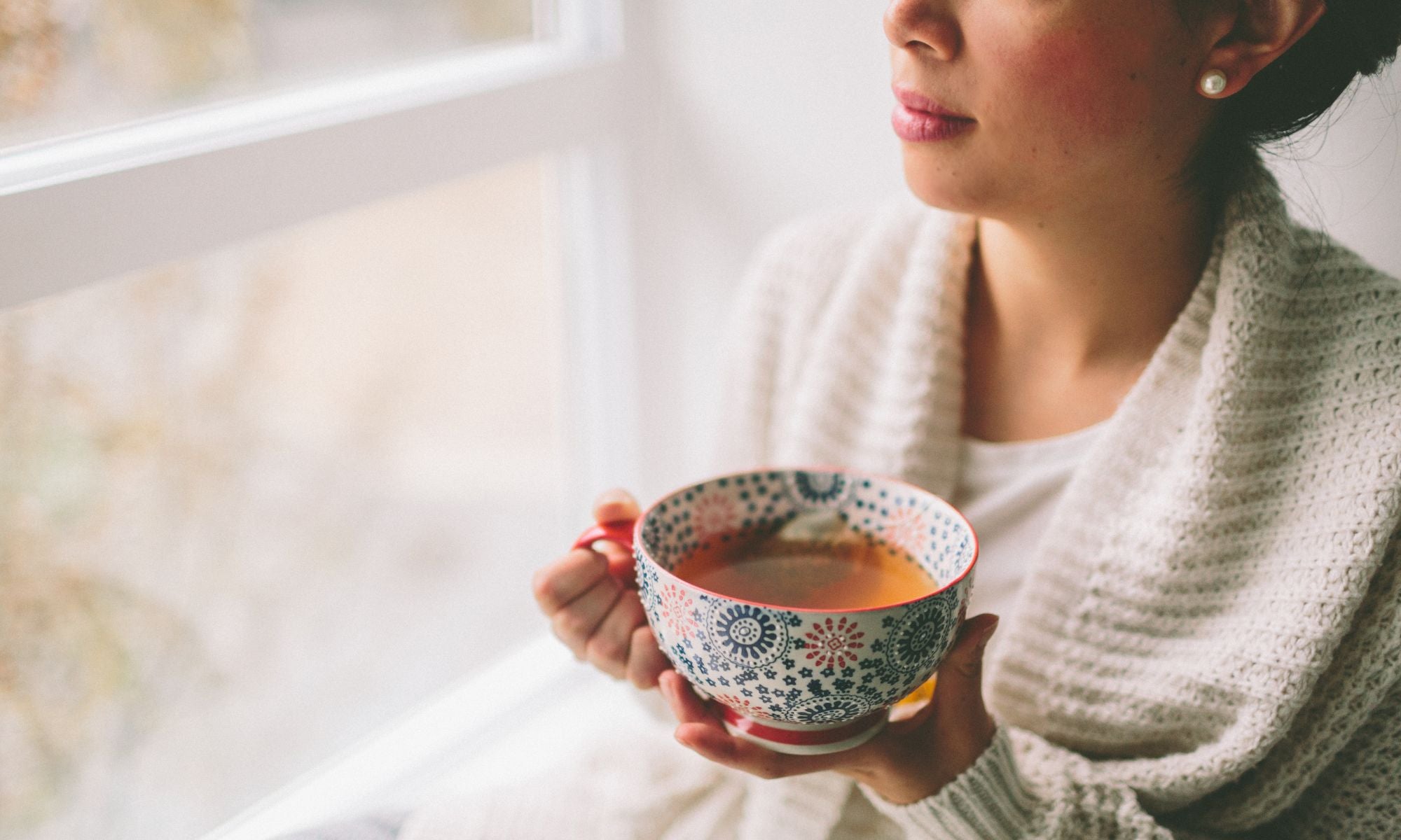 Woman looking out window with cup of tea