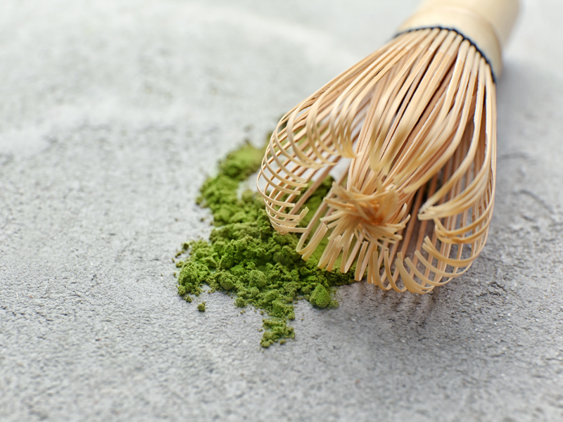 matcha green tea powder on a gray surface with bamboo whisk