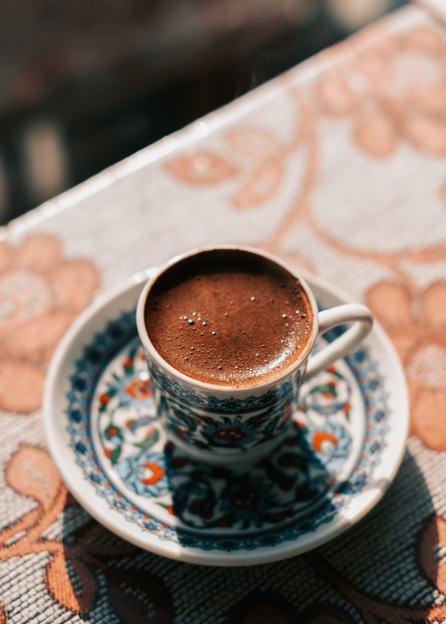 ornate small turkish espresso cup and saucer filled with thick turkish coffee on sunlight ledge with floral placemat