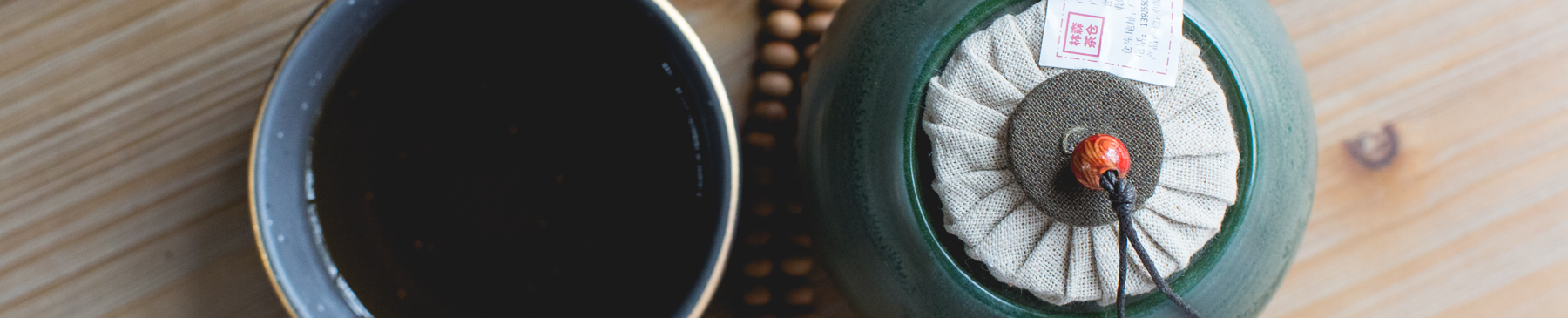 cup of tea next to green clay tea canisters on wood surface with beads